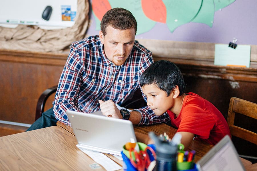 Teacher helping elementary student with STEM project on computer