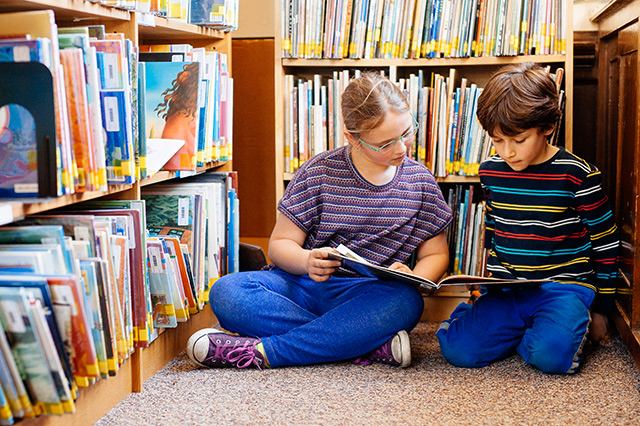 Elementary students reading on floor in library, surrounded by books