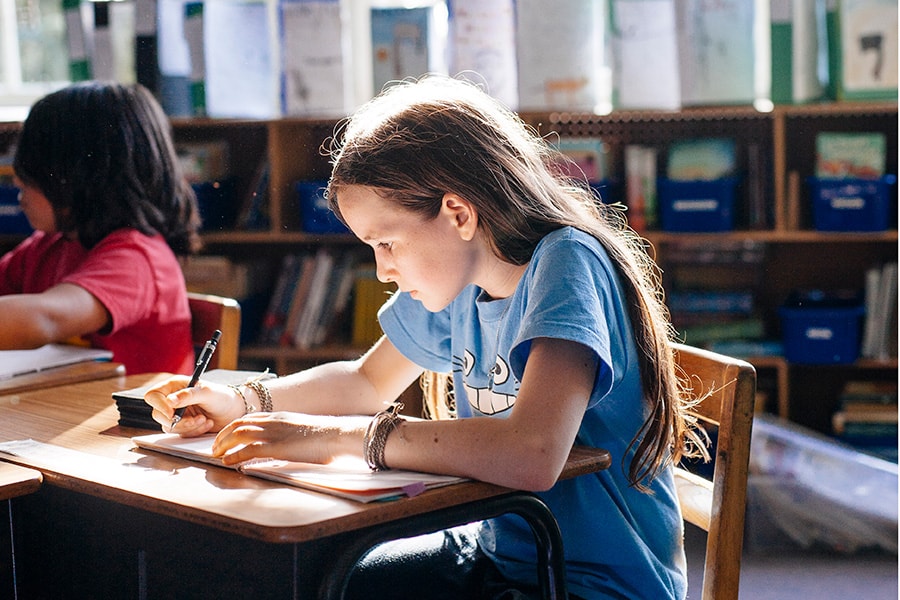 Girl writing in sunny elementary school classroom