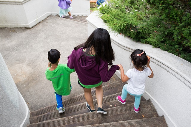 2 younger children holding hands with older child, descending stairs