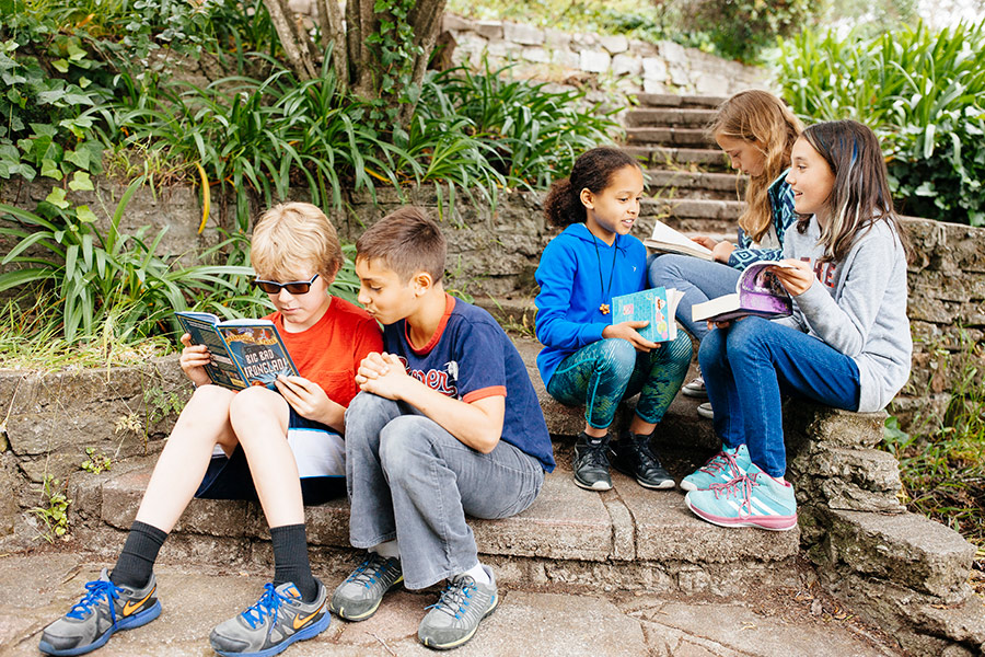 5 elementary school kids reading together outdoors