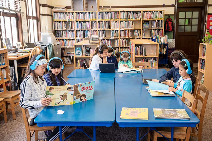 Elementary students reading on floor in library, surrounded by books